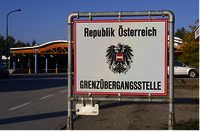 Vor einem Autogrenzübergang steht ein Schild. Auf dieser rechteckigen, weißen Tafel befindet sich in der Mitte der Bundesadler, oben der Schriftzug: Republik Österreich und unten: Grenzübergangsstelle.