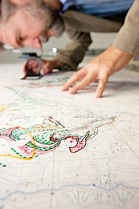Ein Kartograph sieht durch eine Lupe auf eine Manuskriptkarte.
