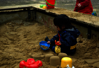 Ein Kind sitzt in der Sandkiste und baut Sandkuchen mit Kübel und Sandformen.
