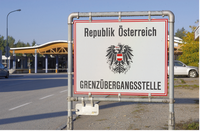 Vor einem Autogrenzübergang steht ein Schild. Auf dieser rechteckigen, weißen Tafel befindet sich in der Mitte der Bundesadler, oben der Schriftzug: Republik Österreich und unten: Grenzübergangsstelle.