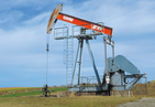 Pumpjack in the form of a horse's head pump. On background blue sky with cirrus clouds and fields.