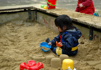 A child sits in the sandbox and build sand cake with bucket and sand molds.